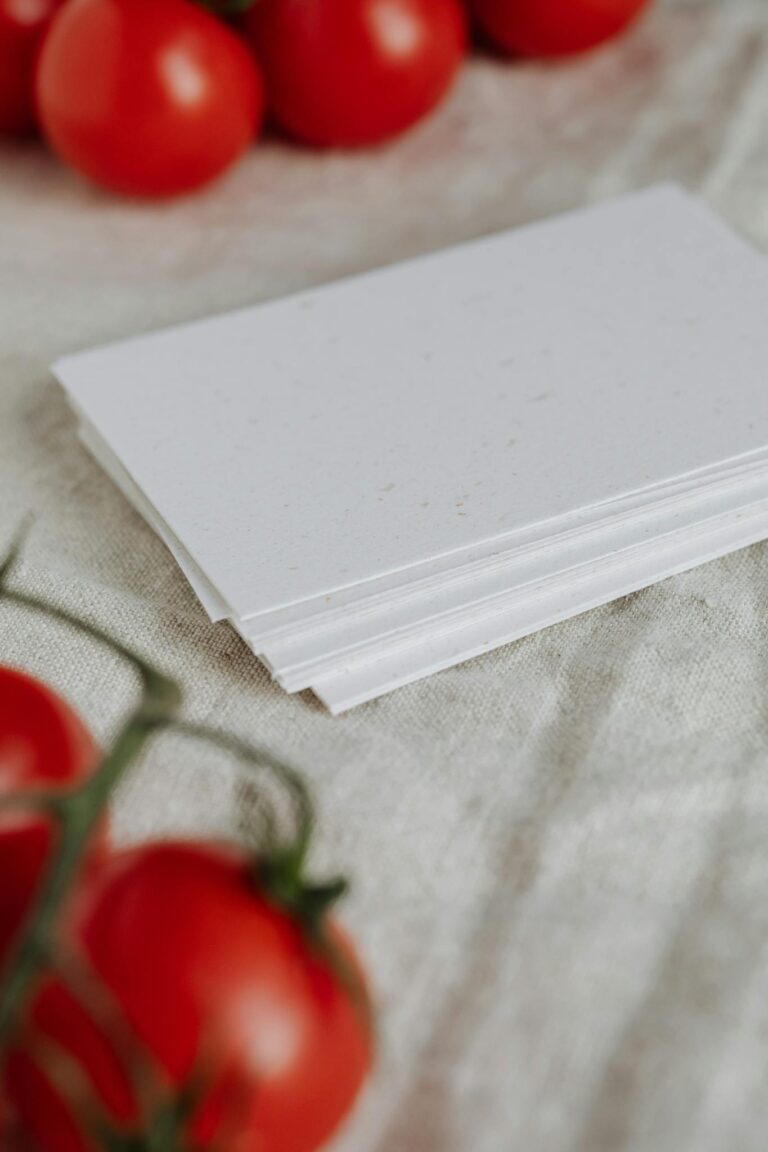 A minimalist stack of white cards surrounded by fresh red tomatoes on a textured cloth.