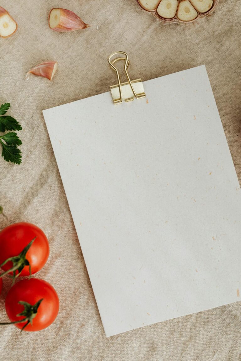 Overhead view of a blank recipe card with fresh tomatoes, garlic, and herbs on a rustic fabric background.