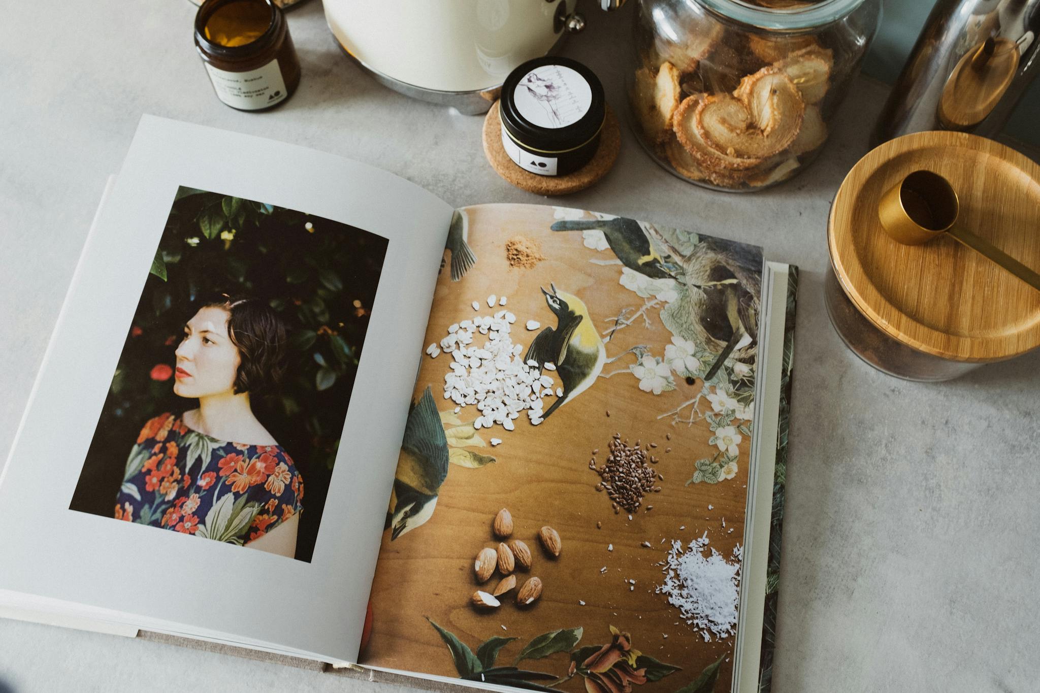 Portrait open book on kitchen counter with jars, spoon, creating a cozy literary vibe.
