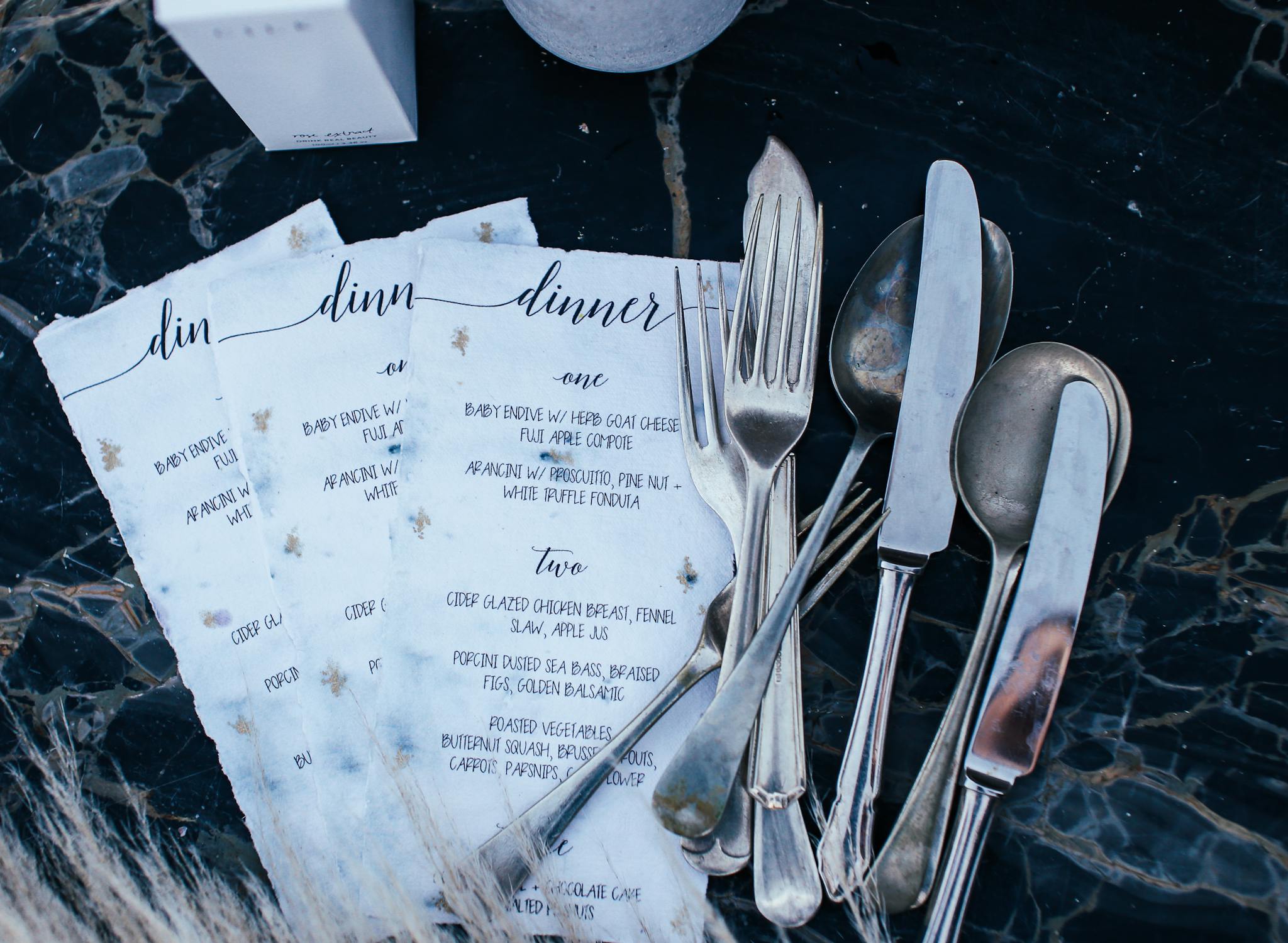 Stylish dinner menus with classic silver cutlery on a patterned marble surface, exuding a vintage vibe.